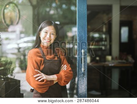 Beautiful Asian Woman Store Owner With Standing In The Doorway Of Her Coffee Shop Looking At Camera 