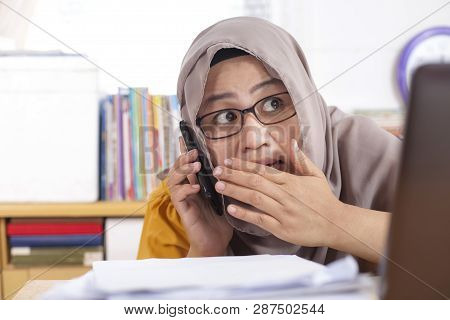 Portrait Of Asian Muslim Businesswoman Is Secretly Talking On The Phone At Work. Leaking Confidentia