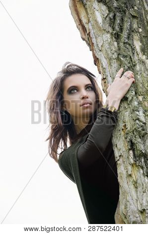 Portrait Of A Woman With Bright Make-up, Peek-a-boo From Behind A Tree On A White Background