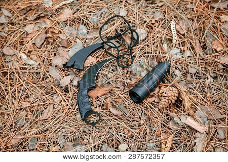 Monocle And Karambit Knife On The Ground Covered With Pine Needles