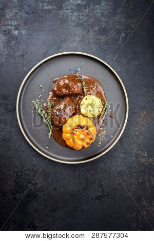 Traditional German braised pork cheeks in brown red wine sauce with fried mushed potatoes and pumpkin as top view on a modern design plate with copy space 