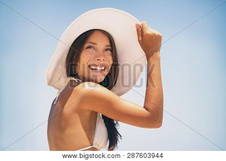 Beach hat Asian bikini woman enjoying sun wearing fashion white hat for solar protection skin care on summer vacation holidays. Young happy people lifestyle.