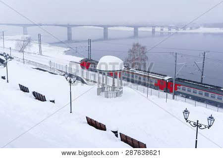 Winter Snowy Landscape With Electric Multiple Unit Train Moving Along The River Bank With A Vintage 