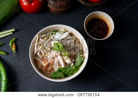 Asian rice noodles soup and chicken in bowl on dark background. Top view flat lay.
