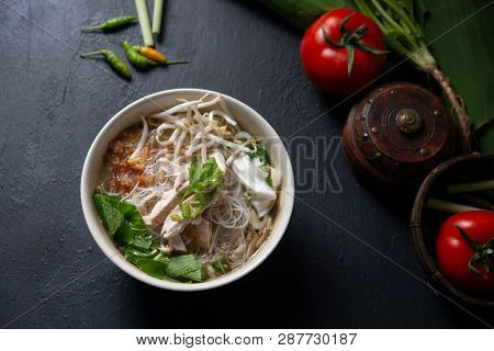 Asian rice noodles soup and chicken in bowl on dark background. Top view flat lay.