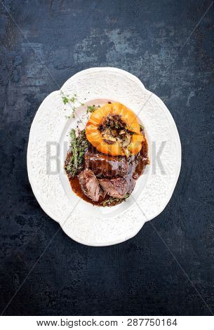 Traditional German braised pork cheeks in brown red wine sauce with mushroom and pumpkin as top view on a shabby chic design white plate with copy space 