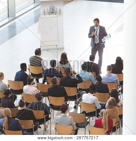 High angle view of Caucasian businessman giving speech at business conference while group of diverse business people listening at conference room.