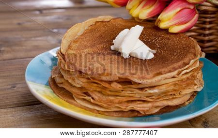 Lots Of Thin Pancakes On A Wooden Background Or Table, And A Basket With Fresh Red-yellow Tulips. Ba
