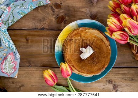 Lots Of Thin Pancakes On A Wooden Background Or Table, And A Basket With Fresh Red-yellow Tulips. Ba