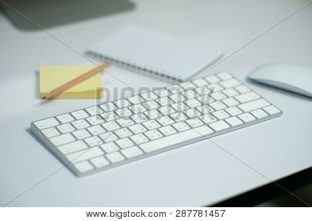 Selective Focus On White Keyborad On The Desk With Defocused Stationary, And Mouse In Background