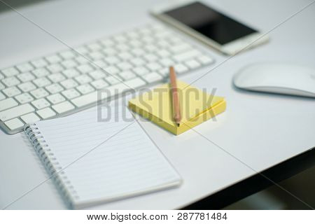 Closeup Wooden Pencil On Blank Paper With Blurred White Keyboard And Stationary In Background.