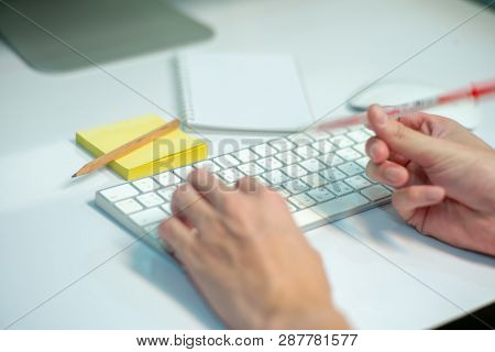 Selective Focus On White Keyboard Of Desk Top With Blurred Motion Of Hands Spinning The Pencil In Fo