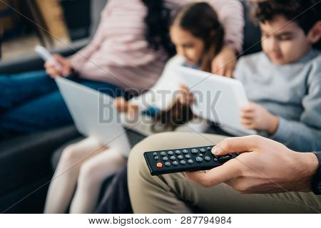 Selective Focus Of Remote Contol In Hand Of Woman Near Hispanic Hamily Using Gadgets