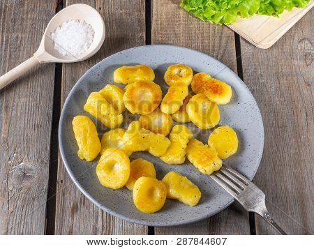 Fried Potato Gnocchina On A Gray Ceramic Plate, Leaves Of Fresh Leaf Lettuce Lie On An Unpainted Kit