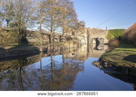 Reflections Of The Ramparts And Trees In Bergues, Northern France, Against A Blue Sky.