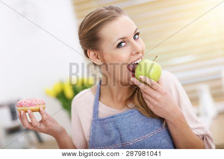 Adult woman choosing between apple and donut in the kitchen