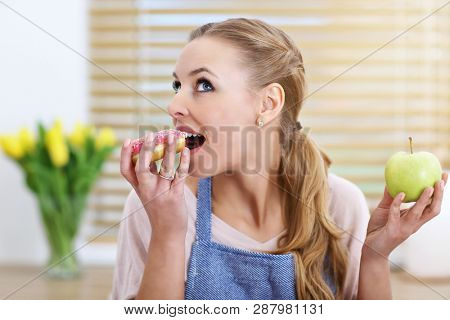 Adult woman choosing between apple and donut in the kitchen