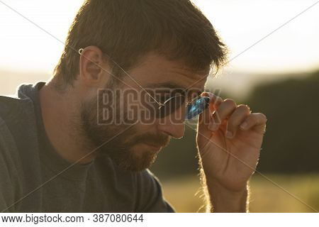 A Young Man Puts On His Sunglasses To See Better At Sunset.