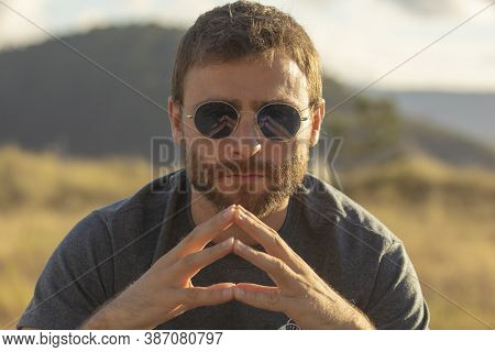 A Young Man, Wearing Glasses, Concentrating On Himself, Meditates In A Relaxed Way, While Enjoying T