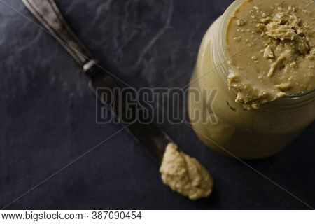 A Messy Jar Of Homemade Peanut Butter In A Glass Jar Sitting On A Dark Gray Slate With An Antique Si