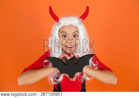 Funny Kid In Witch Costume Hat For Halloween With Devil Hors And Wig Holding Bat On Orange Backgroun