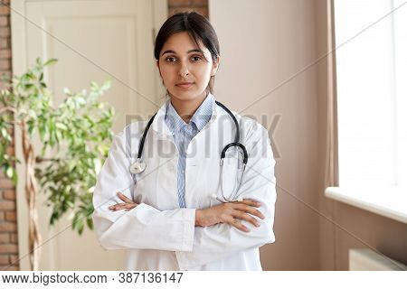 Confident Young Adult Indian Female Doctor Gp Wear White Coat Stethoscope Looking At Camera Standing