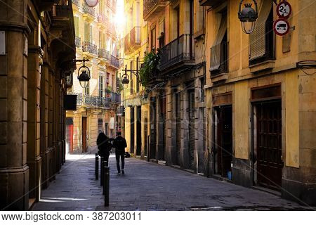 Barcelona, Catalonia, Spain. Romantic narrow residential bystreet in Gothic Quarter. Antique street lamp at wall of old house, parked motorbikes and arch with window between buildings.
