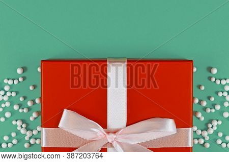 Red Christmas Gift Box With Ribbon Surrounded By Snall White Snowballs At Bottom Of Green Background