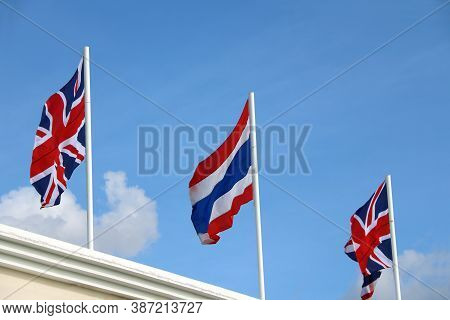 One Of Thai Flag And Two Union Jack Flag On Bright Blue Sky Background. Blown Away By Wind. Two Unit