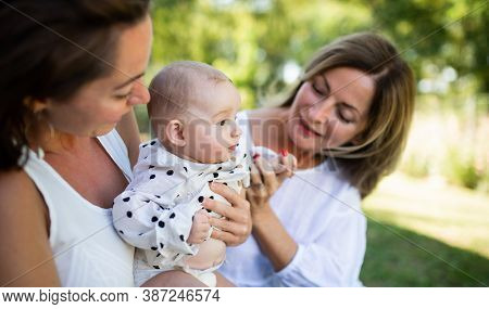 Woman With Daughter And Baby Granddaughter Resting Outdoors In Backyard.