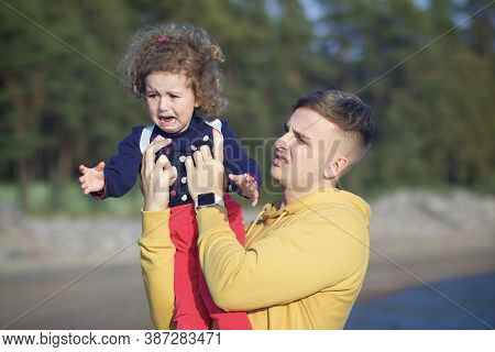 Crying Hysterical Little Girl Kid On Hands Of Her Father. Young Frustrated Angry Man Holding Child O