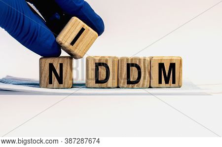 Text Niddm Made From Wooden Cubes. Hands In A Blue Glove.