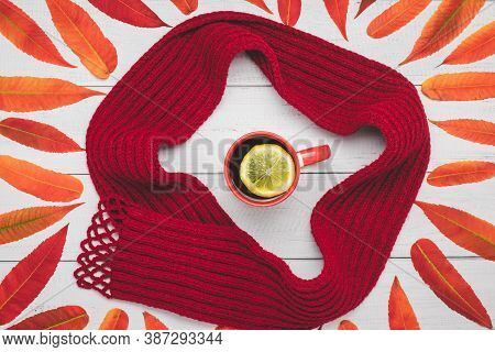 Warm Knitted Scarf And A Red Cup Of Tea With Orange Leaves On A Wood White Table, Autumn Composition