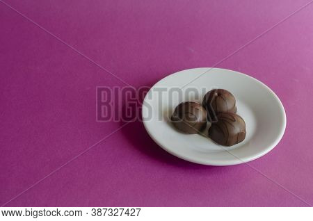 Three Chocolates In A White Porcelain Saucer On A Pink Background. Portion Of Pastry Without Wrapper