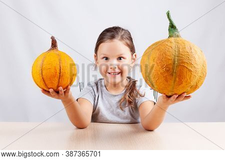 A Happy Child On A White Background Holds Homemade Papier-mache Pumpkins For Halloween