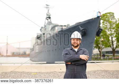 Portrait Of Marine Captain Standing Near Big Vessel In Background, Holding Walkie Talkie.