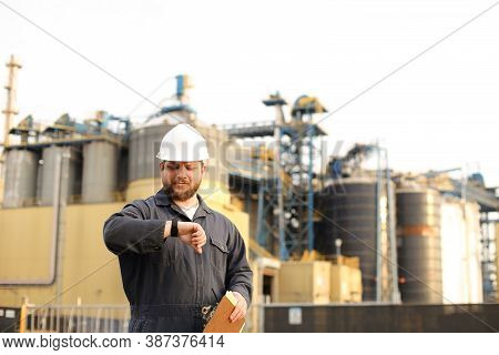 Supervisor Looking At Watch And Holding Papers Notes Near Factory Outside.
