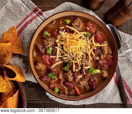 Bowl Of Chili Con Carne With Shredded Ceddar Cheese And Nacho Chips On A Rustic Wooden Table.  Overh