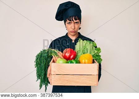 Beautiful brunettte woman chef holding fresh veggetables skeptic and nervous, frowning upset because of problem. negative person. 