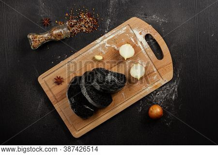fresh black rye bread on a cutting board with seasonings sprinkled with flour on a black wooden tabl