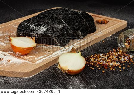 Fresh Black Rye Bread On A Cutting Board With Seasonings Sprinkled With Flour On A Black Wooden Tabl