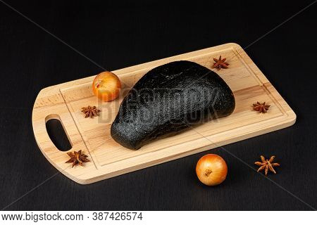 Fresh Black Rye Bread On A Cutting Board With Seasonings Sprinkled On A Black Wooden Table