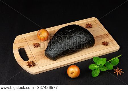 fresh black rye bread on a cutting board with seasonings sprinkled with flour on a black wooden tabl