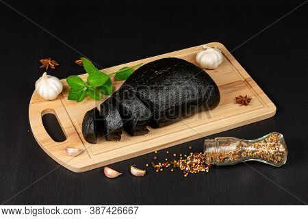 fresh black rye bread on a cutting board with seasonings sprinkled with flour on a black wooden tabl