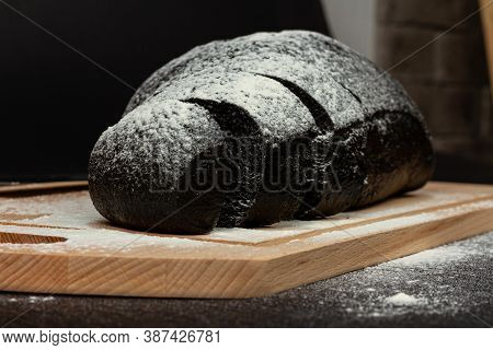 Fresh Black Rye Bread On A Cutting Board With Flour On A Black Wooden Table