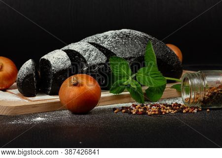 Fresh Black Rye Bread On A Cutting Board With Seasonings Sprinkled With Flour On A Black Wooden Tabl