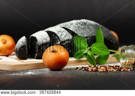 Fresh Black Rye Bread On A Cutting Board With Seasonings Sprinkled With Flour On A Black Wooden Tabl