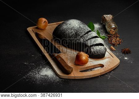 Fresh Black Rye Bread On A Cutting Board With Seasonings Sprinkled With Flour On A Black Wooden Tabl