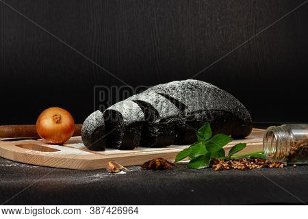 Fresh Black Rye Bread On A Cutting Board With Seasonings Sprinkled With Flour On A Black Wooden Tabl
