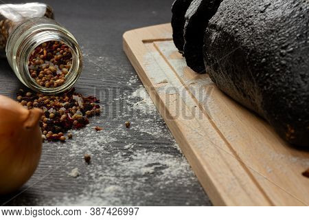 Fresh Black Rye Bread On A Cutting Board With Seasonings Sprinkled With Flour On A Black Wooden Tabl